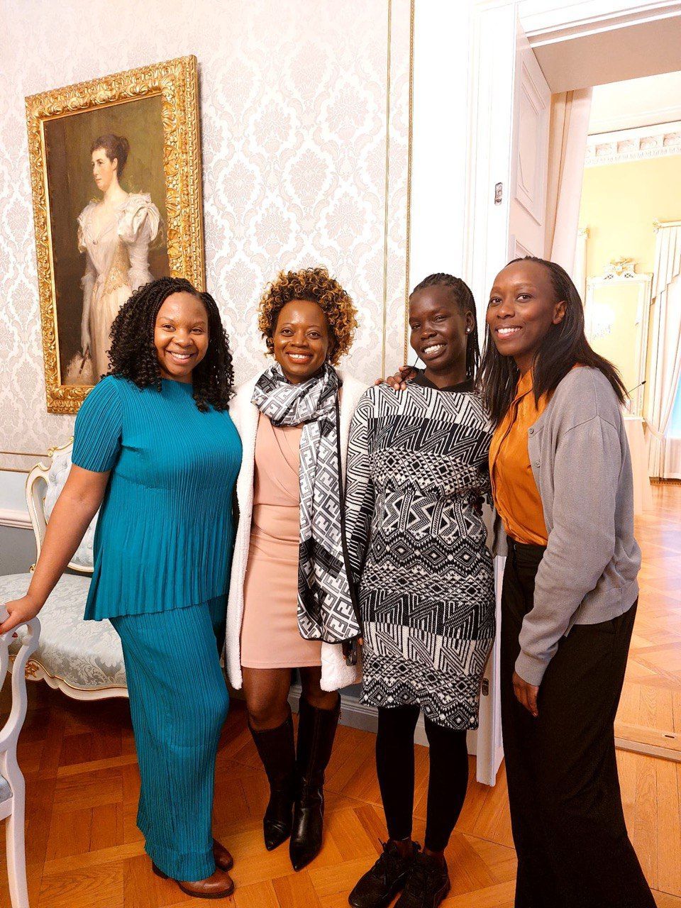 Four women are posing for a picture in front of a painting