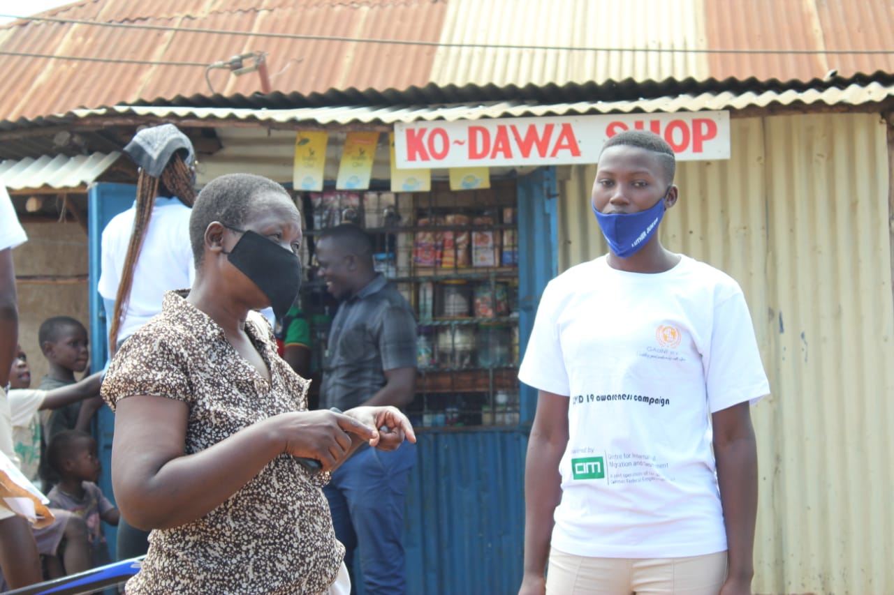 A woman wearing a mask stands in front of a ko dawa shop