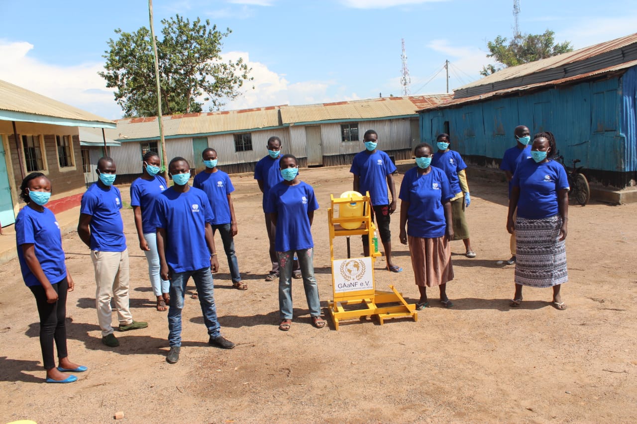 A group of people wearing face masks are standing in a dirt field.