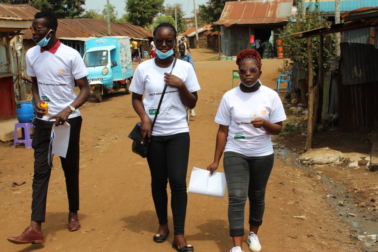 Three people wearing masks are walking down a dirt road.