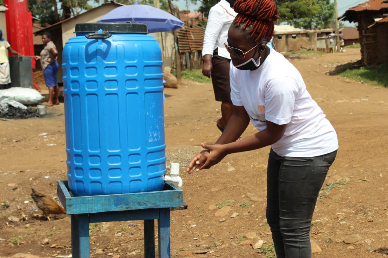 A woman is washing her hands in front of a blue barrel