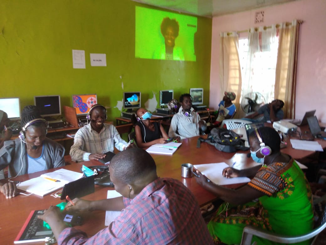 A group of people are sitting around a table in front of a projector screen