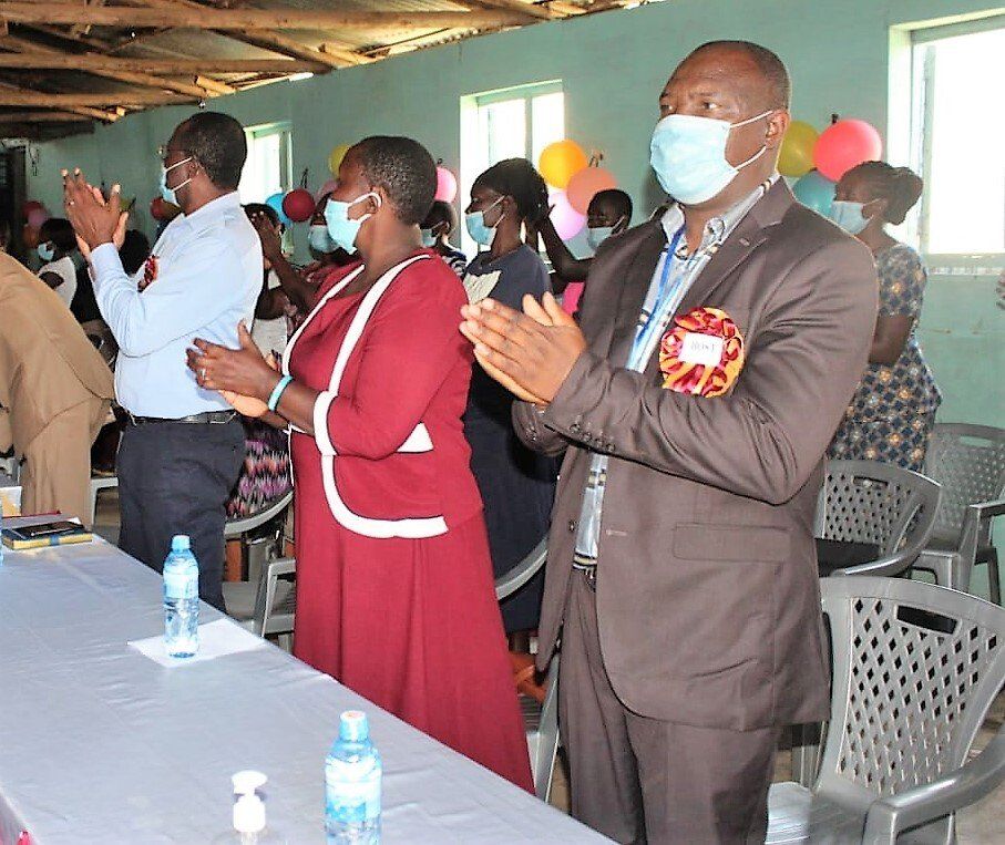 A group of people wearing face masks are clapping in a room