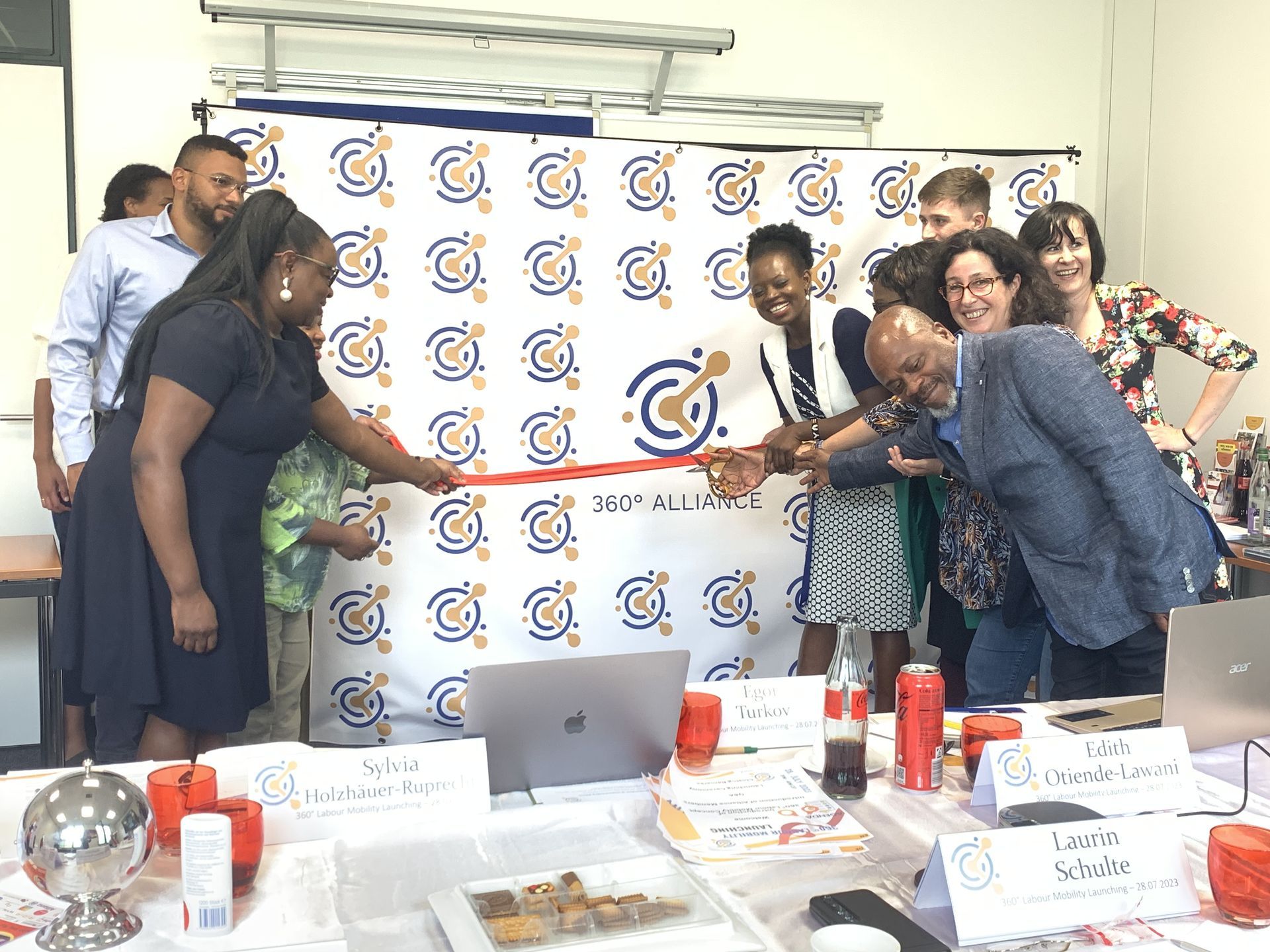 A group of people are standing around a table cutting a red ribbon.