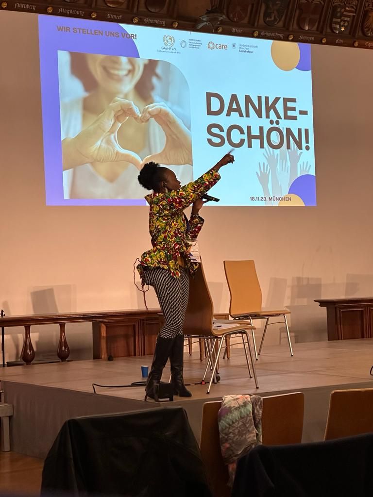 A woman is singing into a microphone in front of a screen that says danke-schon