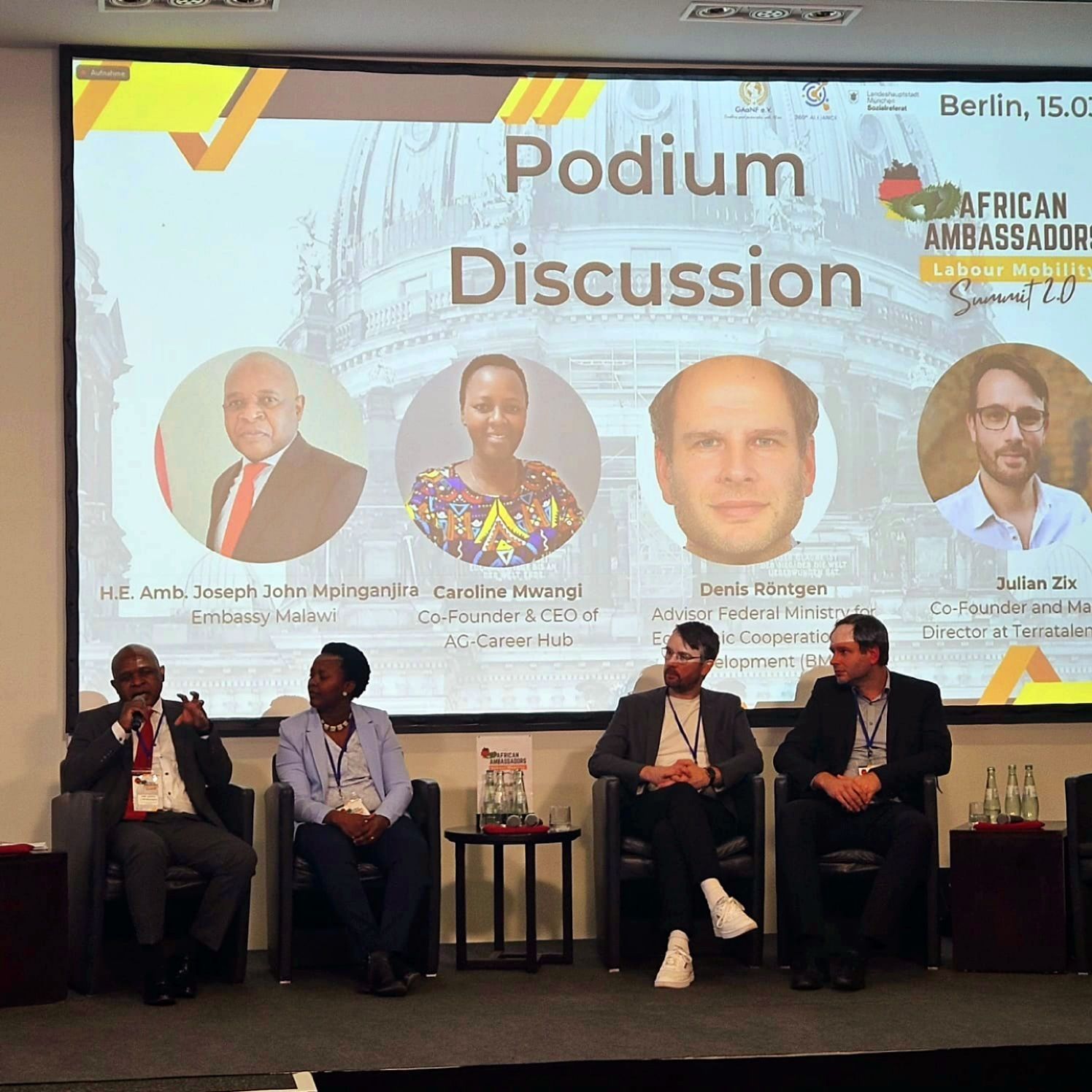 A group of people sitting in front of a large screen that says podium discussion