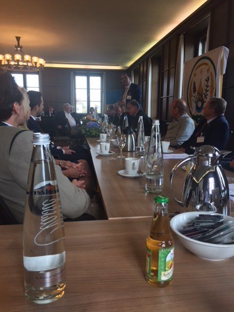 A group of people are sitting at a long table with a bottle of orange juice on the table