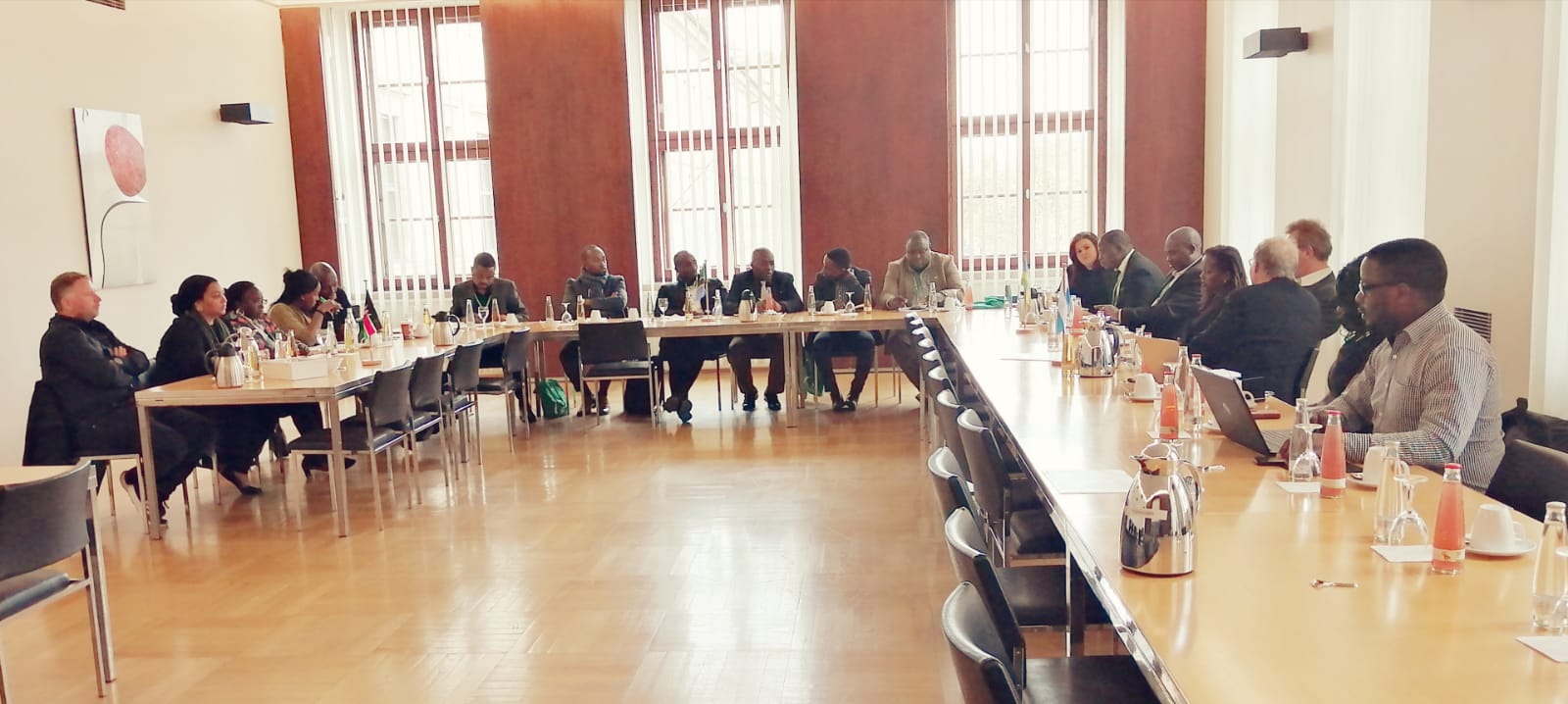 A group of people are sitting at long tables in a conference room.