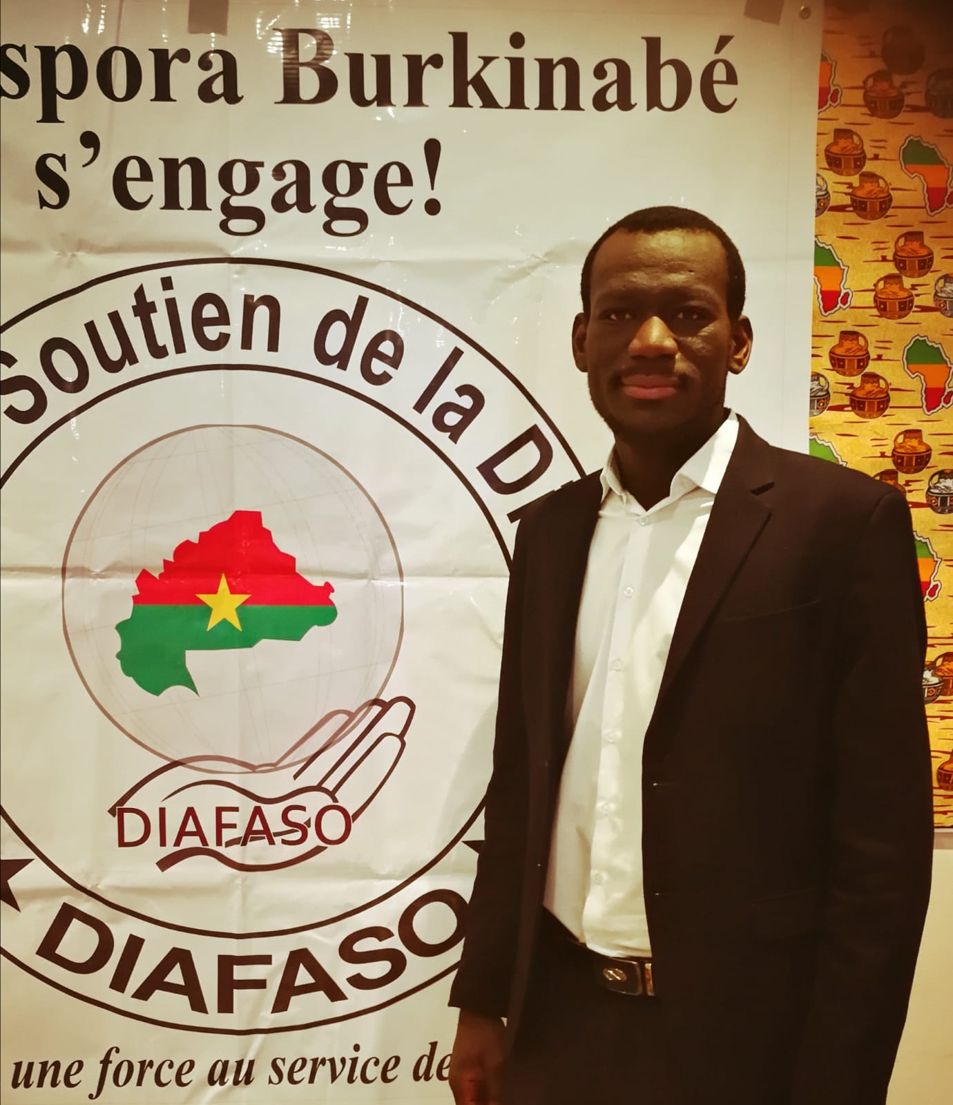 A man in a suit stands in front of a sign that says spora burkinabe s ' engage