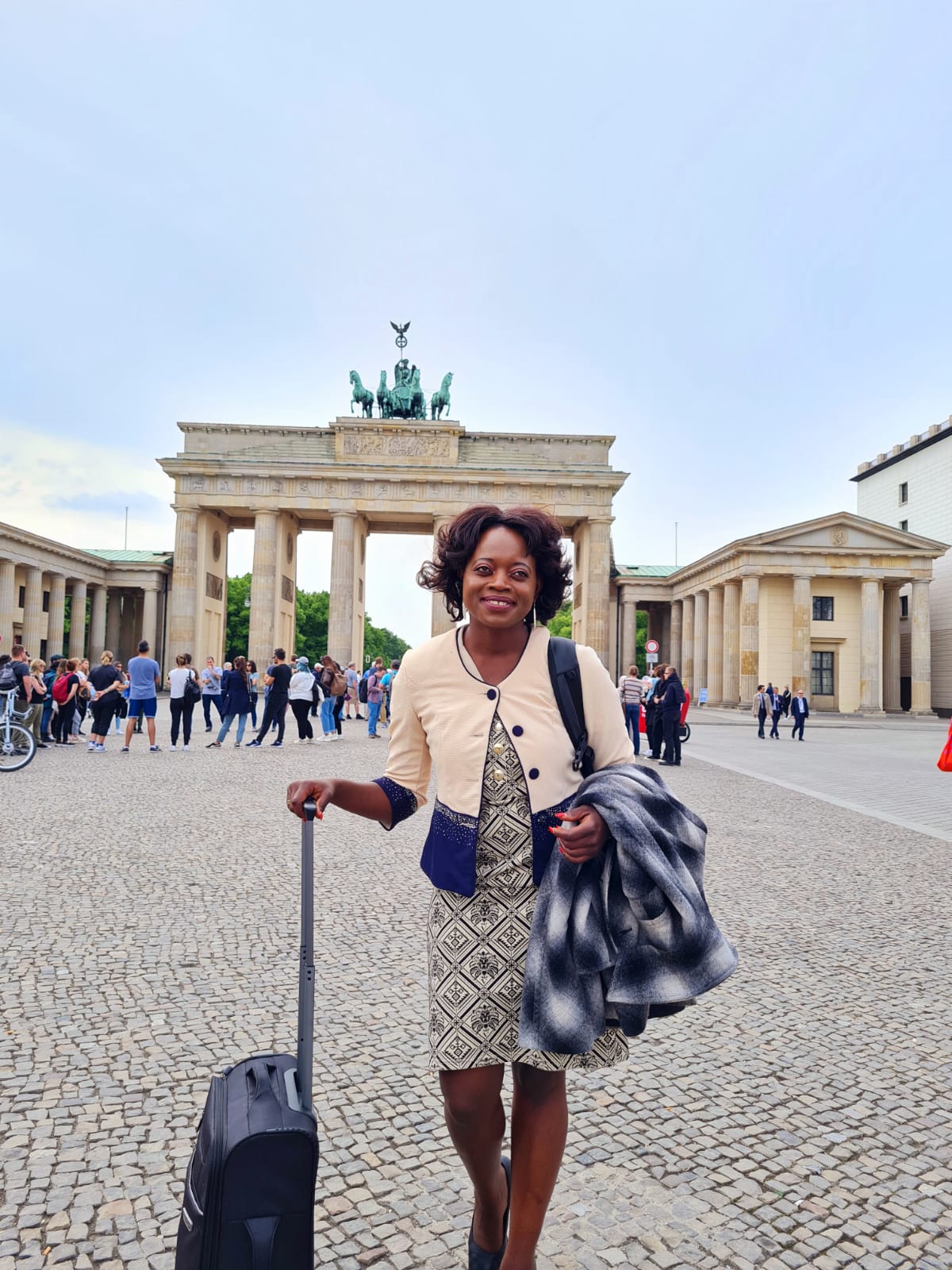 A woman is holding a suitcase in front of a large building.