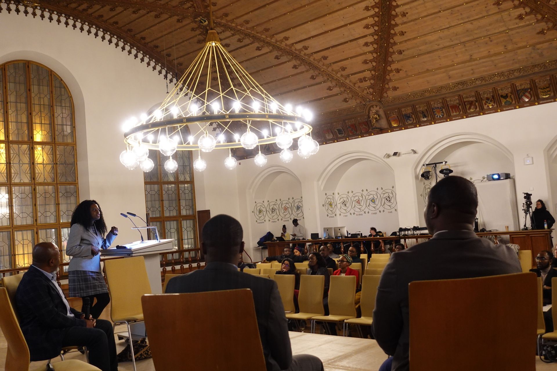 A group of people are sitting in a room with a chandelier hanging from the ceiling