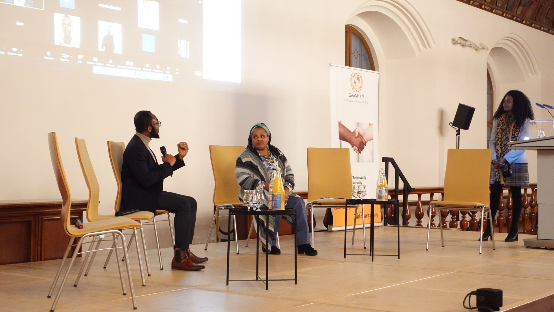 A group of people are sitting in chairs on a stage talking to each other.