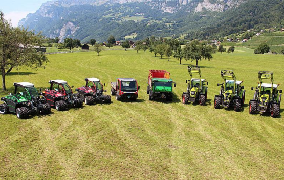 A row of tractors are parked in a grassy field.