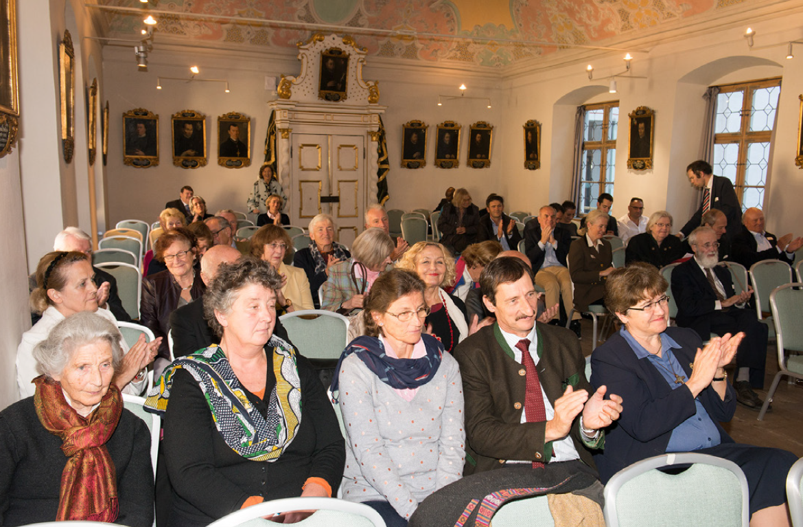 A large group of people are sitting in chairs in a room applauding.