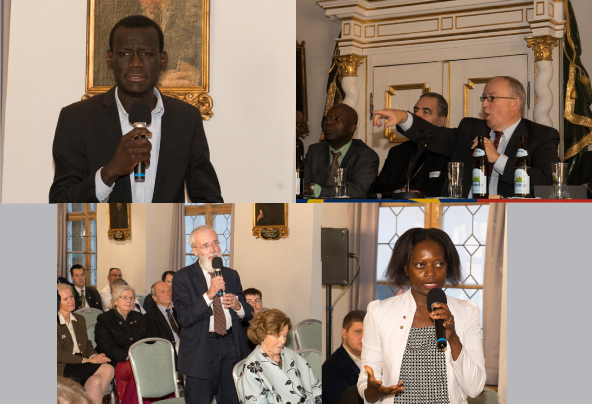 A man in a suit is speaking into a microphone in front of a group of people