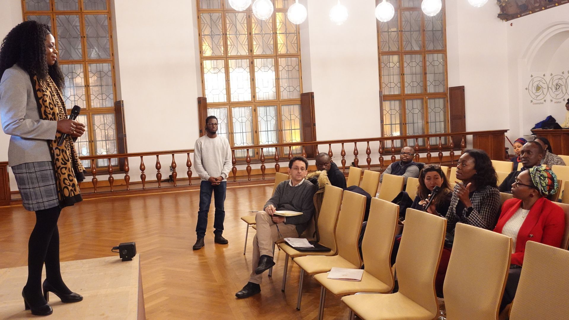 A woman is standing in front of a group of people sitting in chairs.