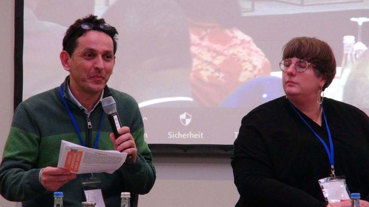 A man is speaking into a microphone while a woman looks on.