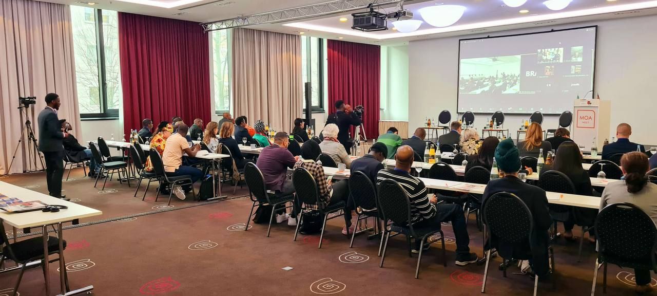 A group of people are sitting at tables in a conference room.