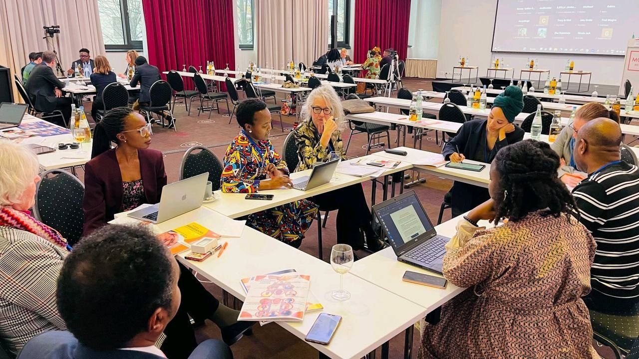 A group of people are sitting at tables in a room with laptops.