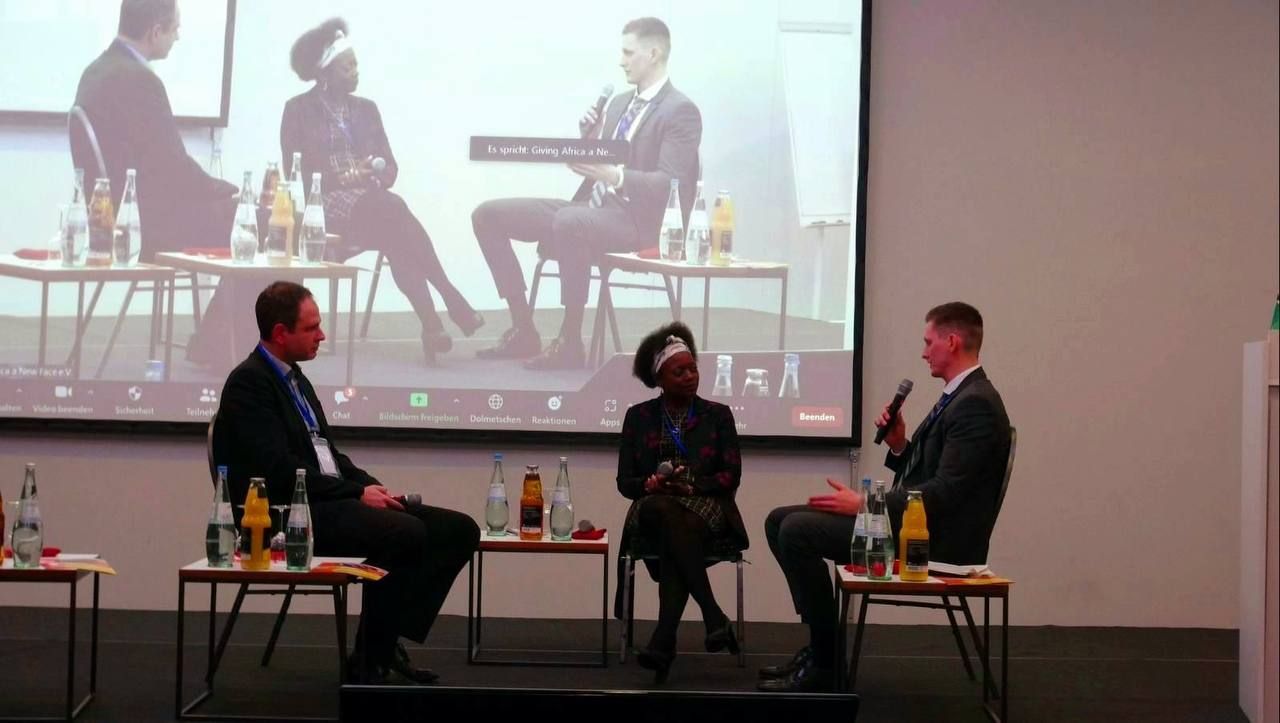 A group of people are sitting at tables in front of a large screen.
