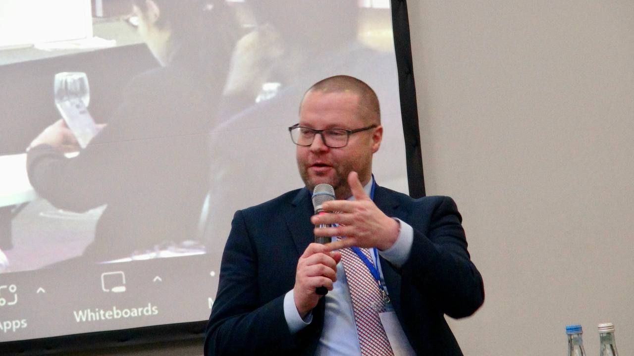 A man in a suit and tie is holding a microphone in front of a screen.