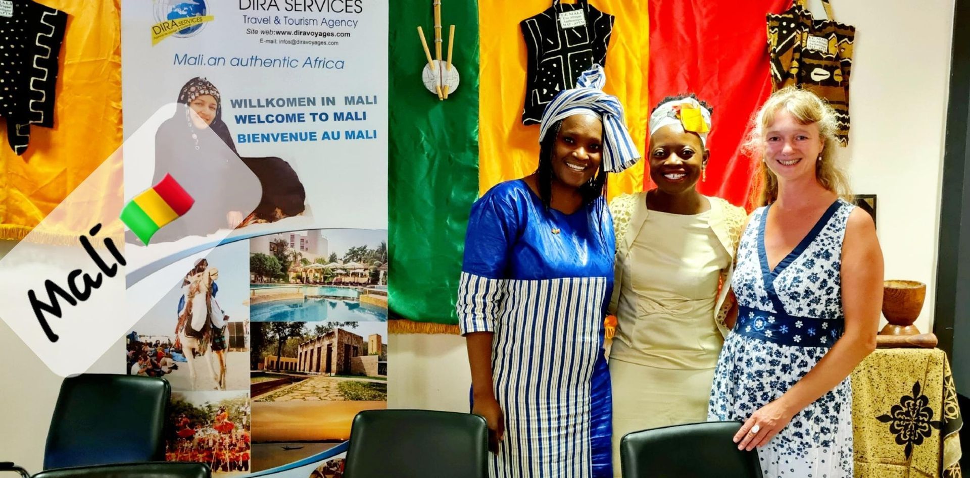 Three women are posing for a picture in front of a sign that says mali