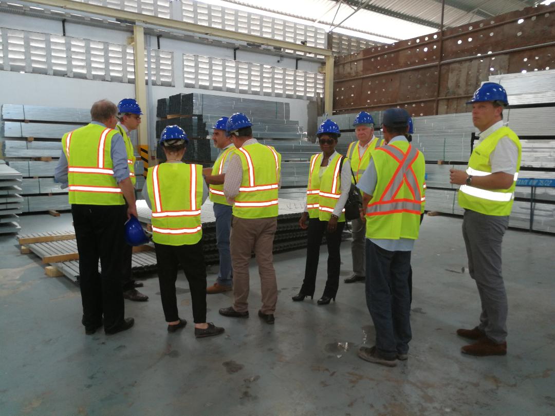 A group of people wearing hard hats and safety vests are standing in a warehouse.
