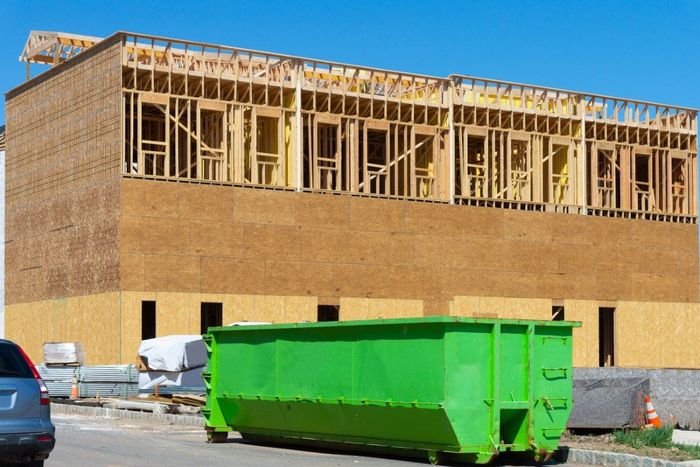 Green dumpster in front of a building under construction; wooden frame visible.