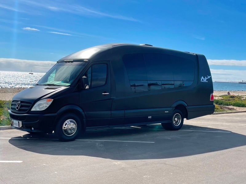 A black van is parked in a parking lot next to the ocean.