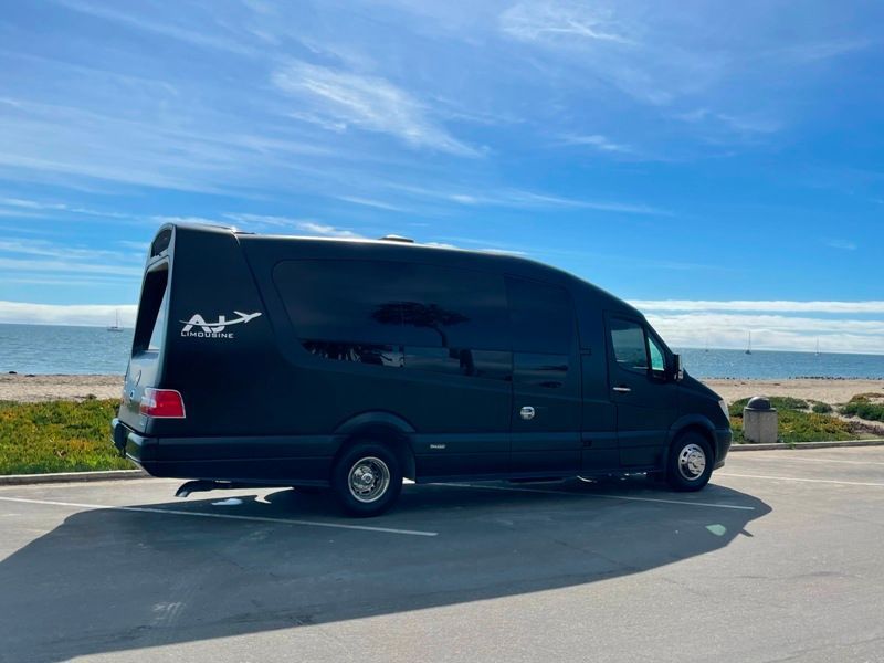 A black van is parked in a parking lot near the ocean.