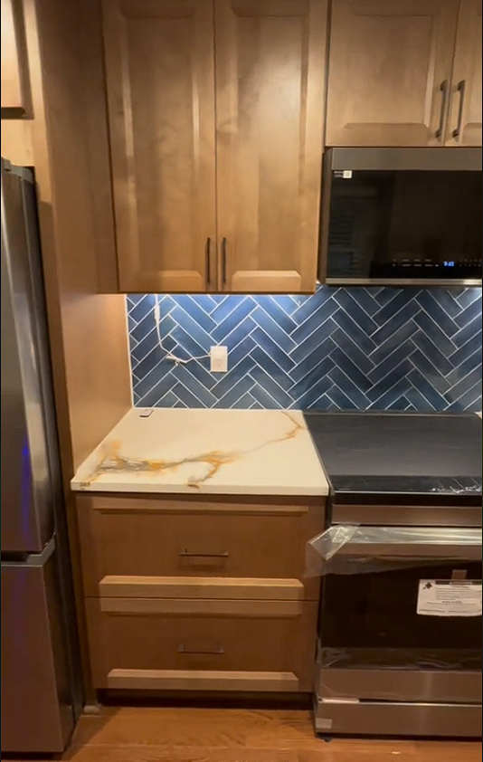 A kitchen with stainless steel appliances , wooden cabinets , a stove , microwave and refrigerator.