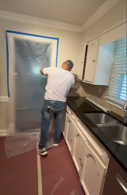 A man in a white shirt is painting a kitchen