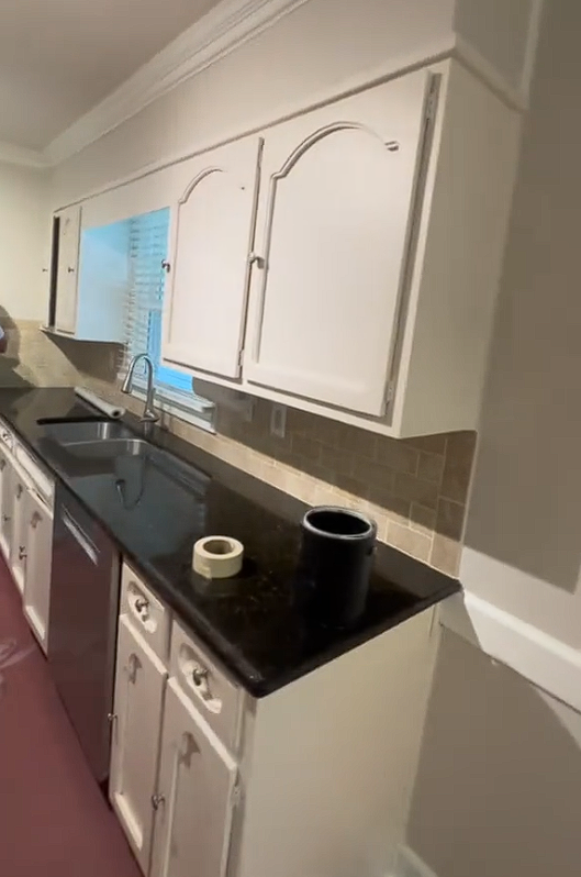 A kitchen with white cabinets , black counter tops , a sink and a dishwasher.