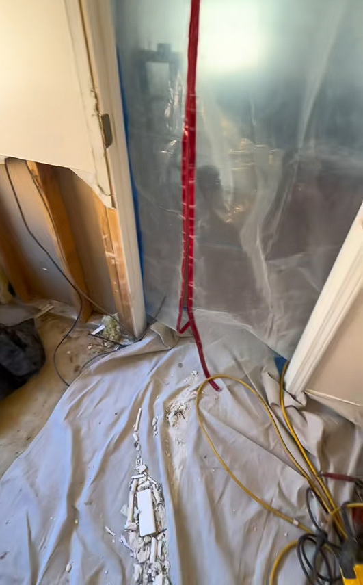 A room with a hole in the wall and a tarp on the floor.