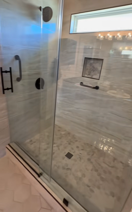 A bathroom with a walk in shower with a glass door.