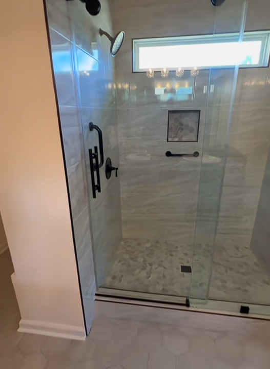 A bathroom with a walk in shower with a glass door and a window.