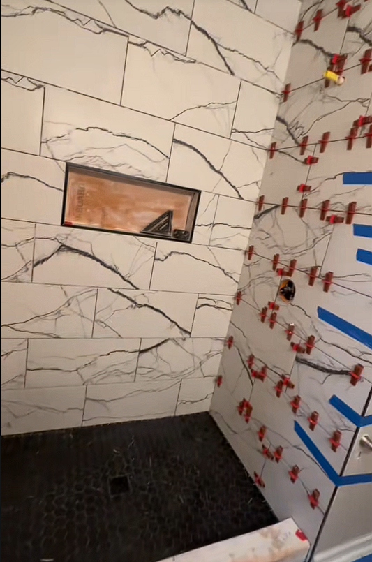 A bathroom with white tiles and a black floor is being remodeled.