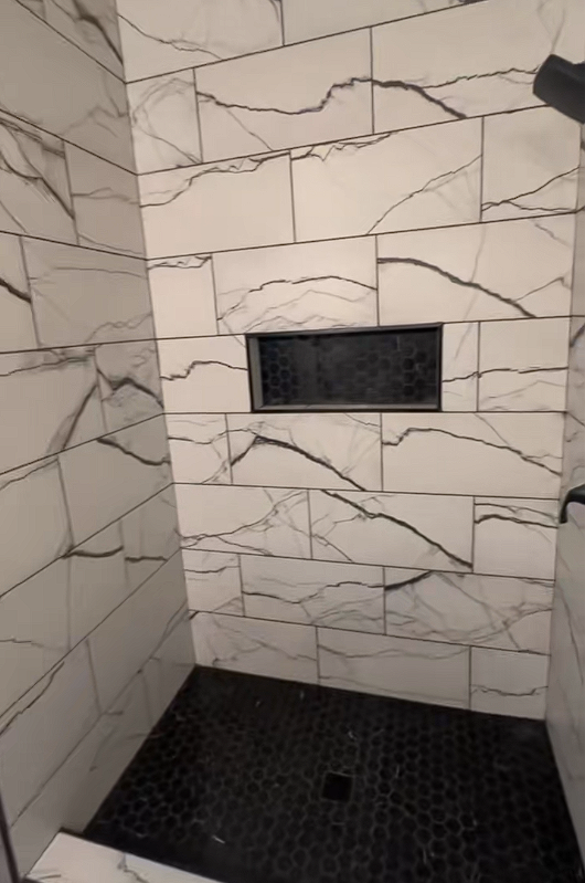 A shower with white tiles and a black floor.