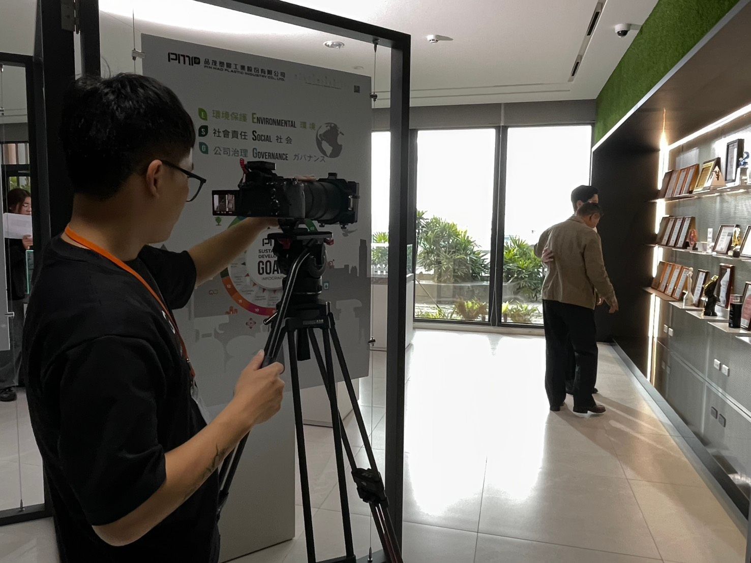 有人在店內用三腳架架著相機拍攝。一名男子正在瀏覽牆上的商品展示。