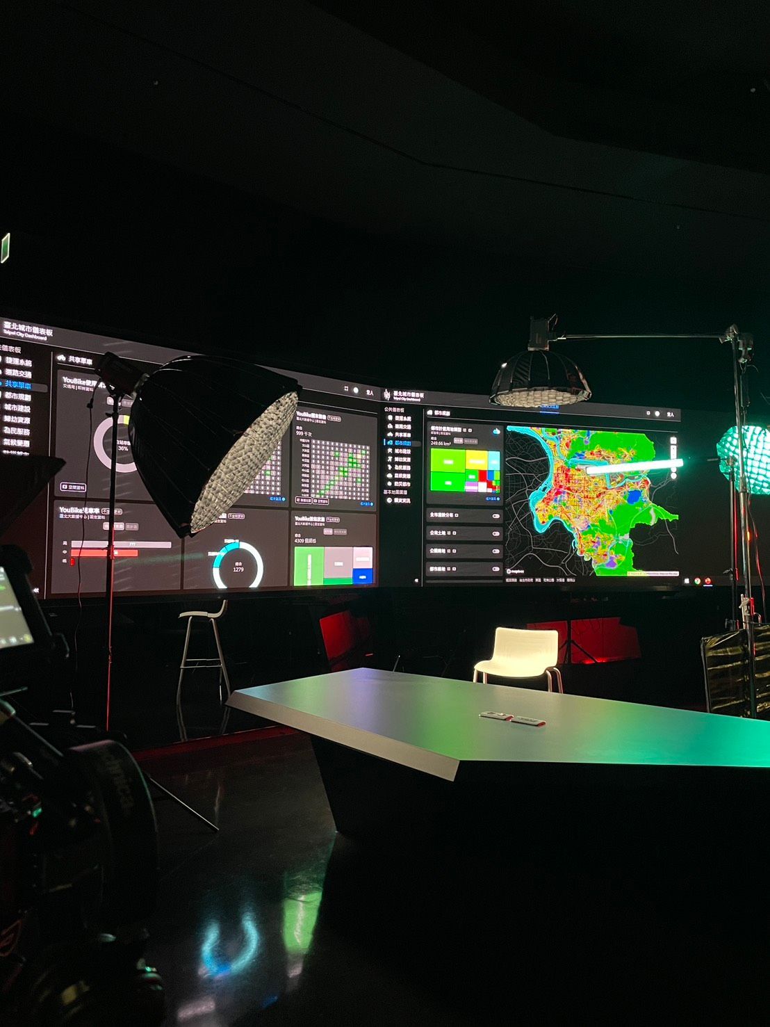 新聞攝影棚配有顯示數據和地圖的大螢幕、一張桌子、燈光和一張凳子。