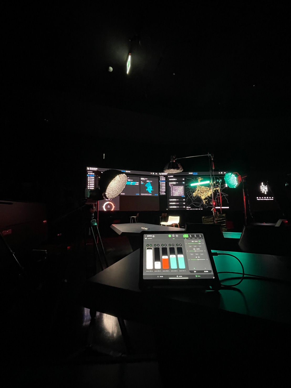 在光線昏暗的控制室裡，前景是一台顯示音訊電平的平板電腦，背景是顯示圖形的電腦顯示器。