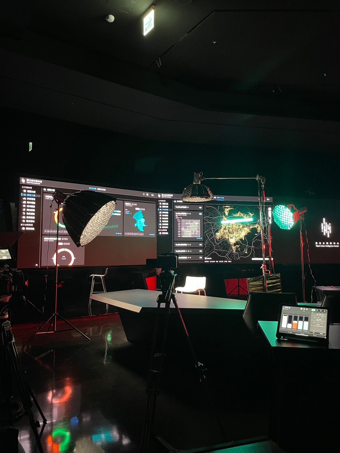 昏暗的攝影棚裡擺放著大型螢幕，上面顯示著數據，還有攝影機和照明設備。