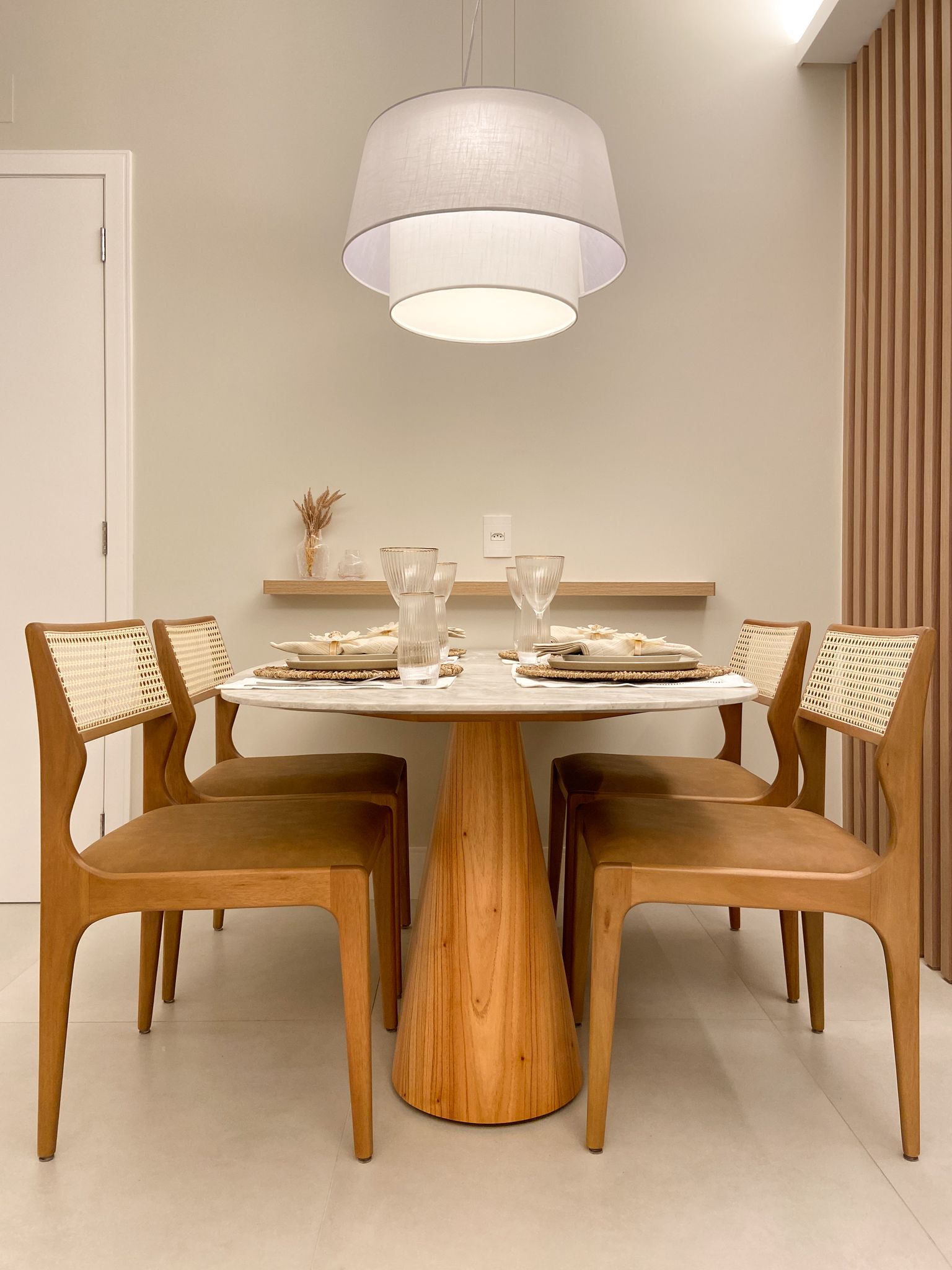 Sala de jantar com mesa redonda de mármore, cadeiras de madeira e luminária pendente.