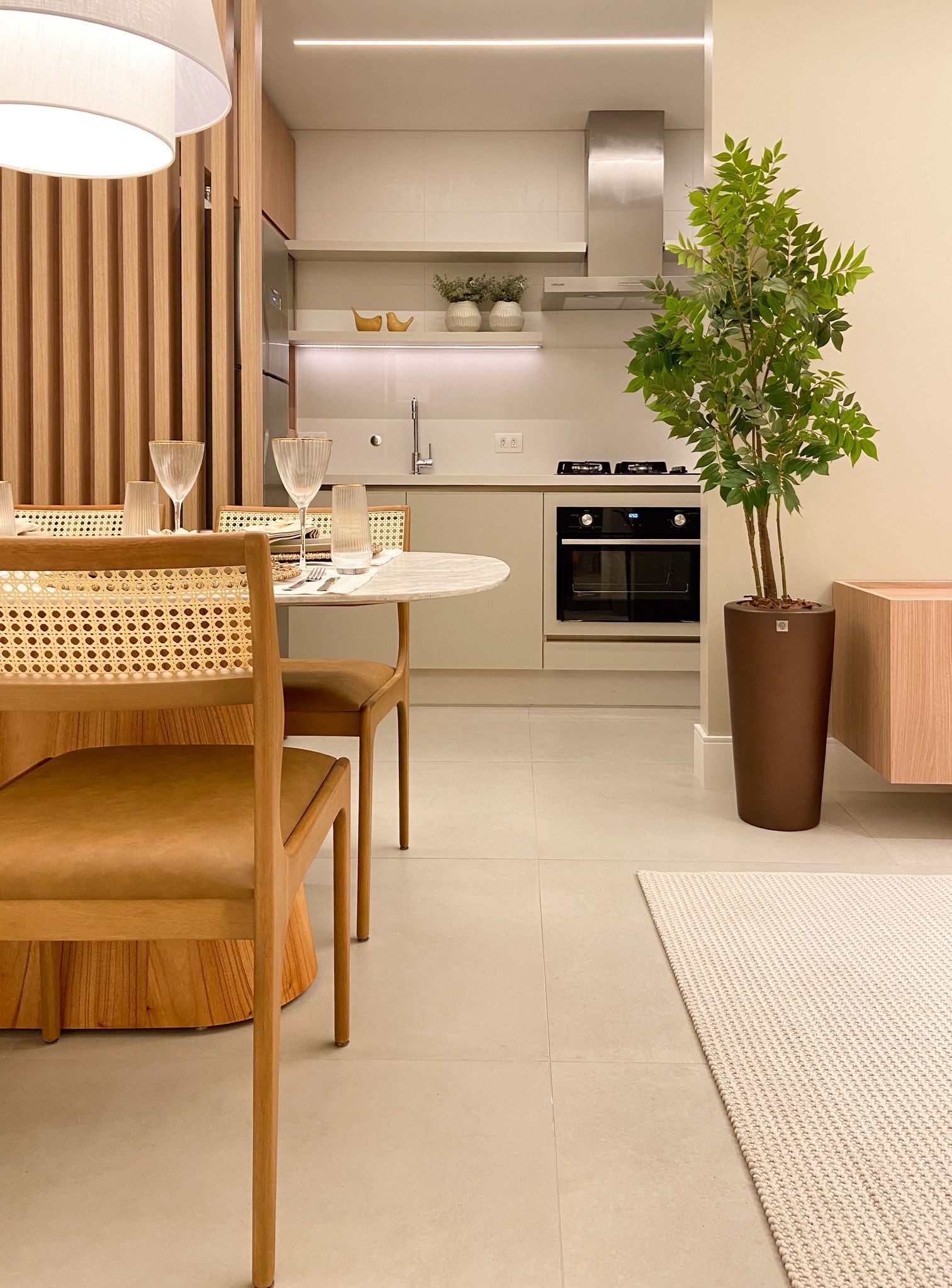 Sala de jantar com cozinha ao fundo. Madeira clara e tons neutros criam um espaço moderno e aconchegante.