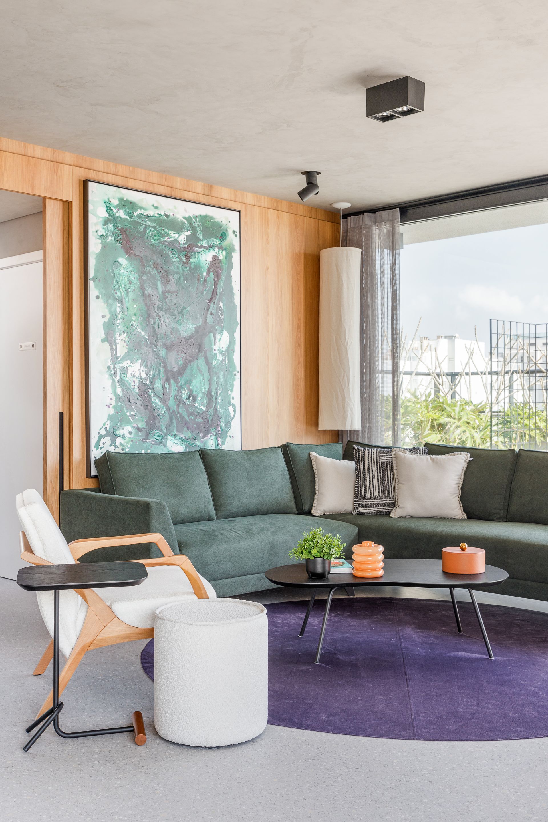 Sofá secional verde em uma sala de estar moderna com um tapete roxo e arte abstrata.