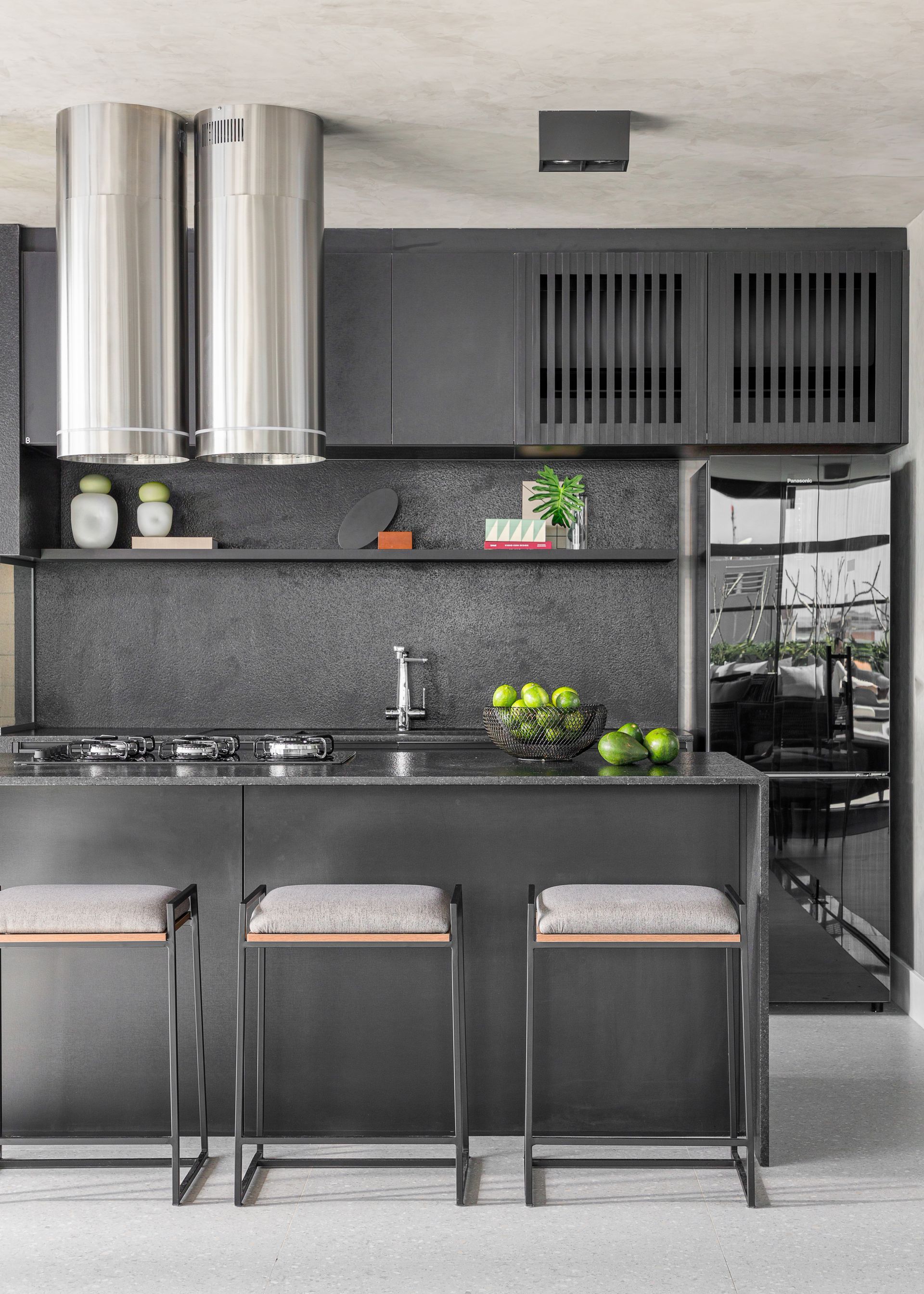 Cozinha moderna em cinza escuro com ilha, bancos, exaustor de aço inoxidável e geladeira integrada.