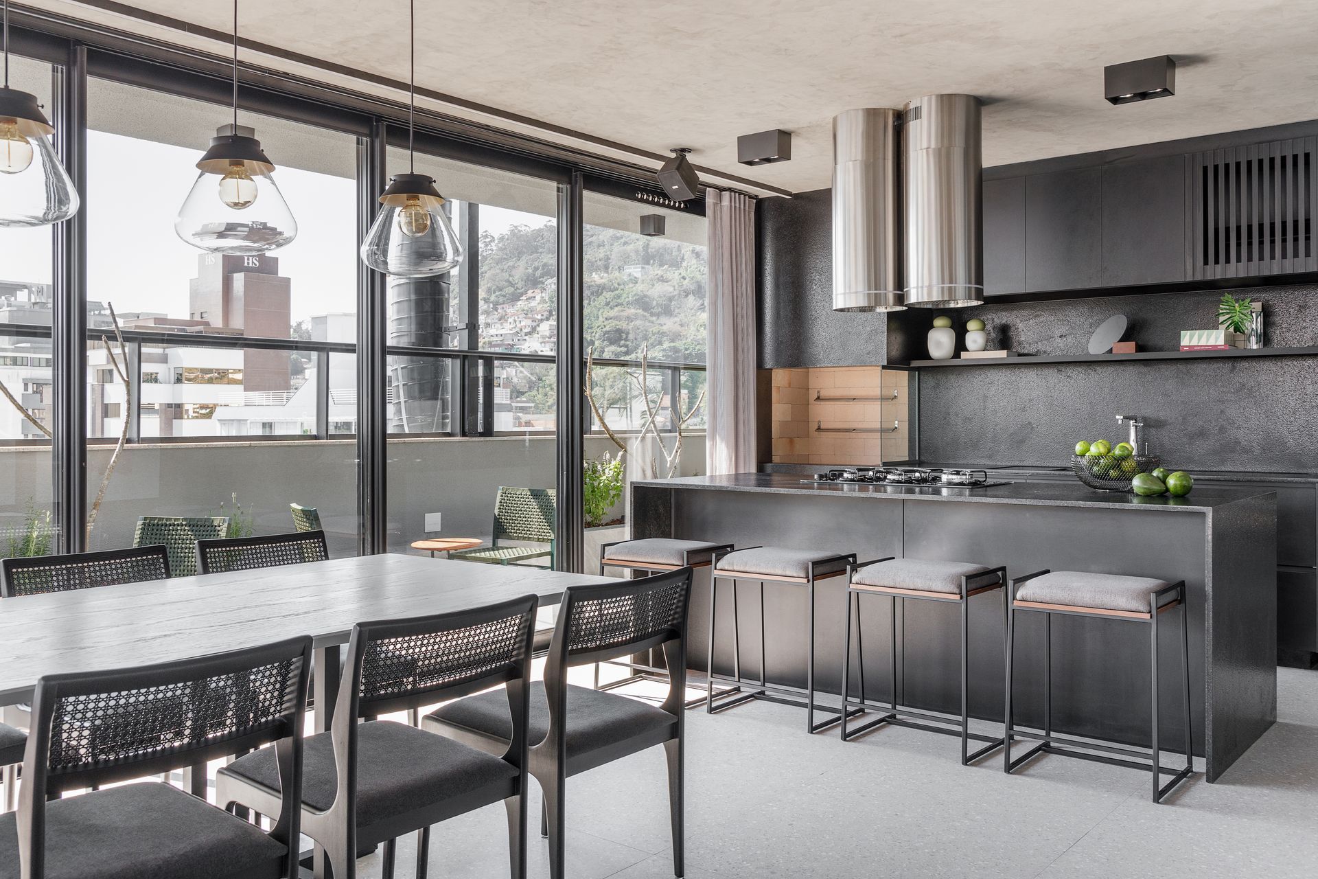 Cozinha moderna com armários escuros, ilha e mesa de jantar. Janelas amplas com vista para a cidade.
