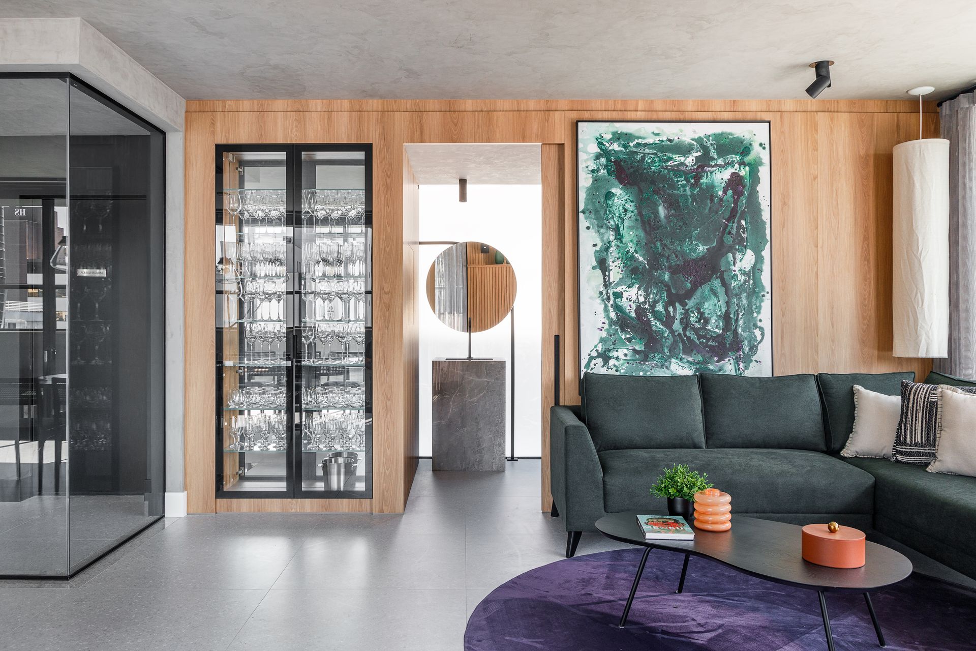Sala de estar moderna com um sofá verde escuro, obras de arte e um armário para vinhos.