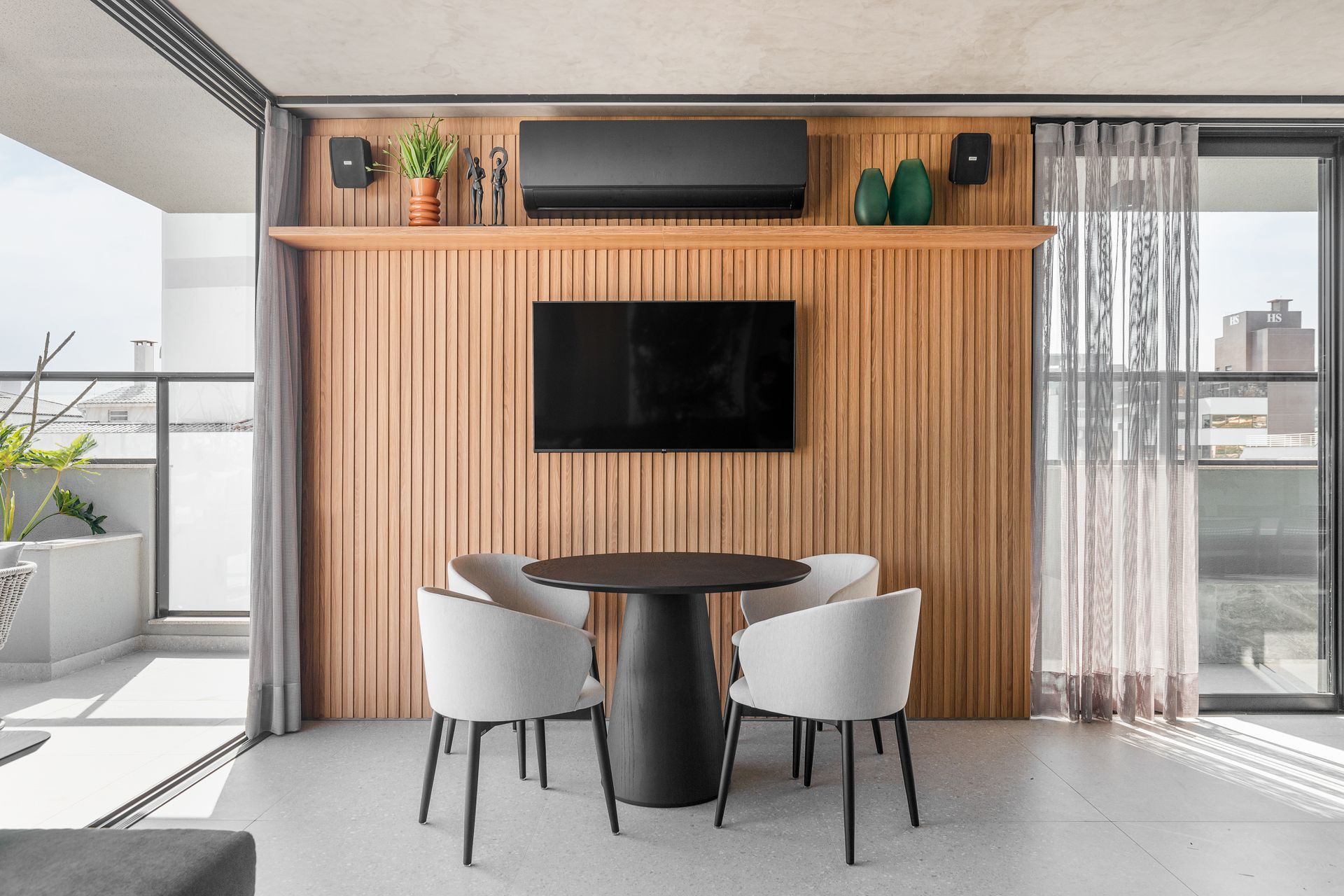 Uma área de jantar com uma mesa redonda e quatro cadeiras, uma TV e uma parede com painéis de madeira.