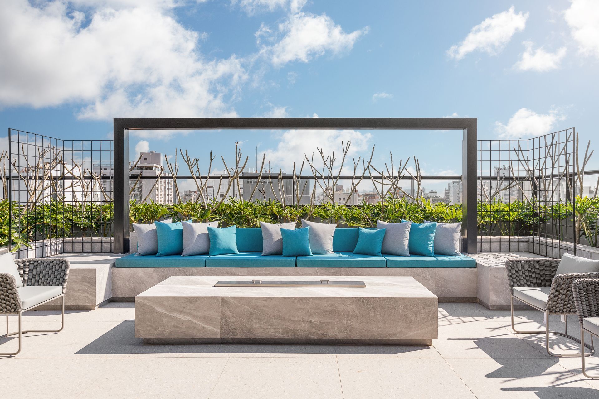 Pátio na cobertura com almofadas turquesa, fogueira e móveis modernos contra um céu azul.